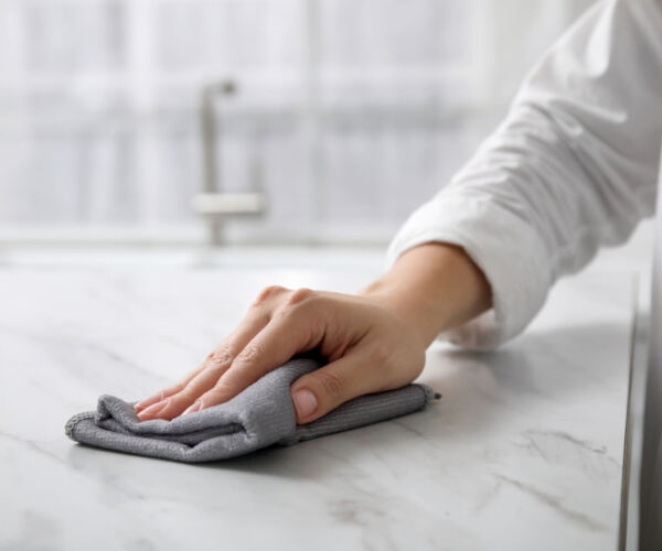 Woman wiping white marble table indoors, closeup